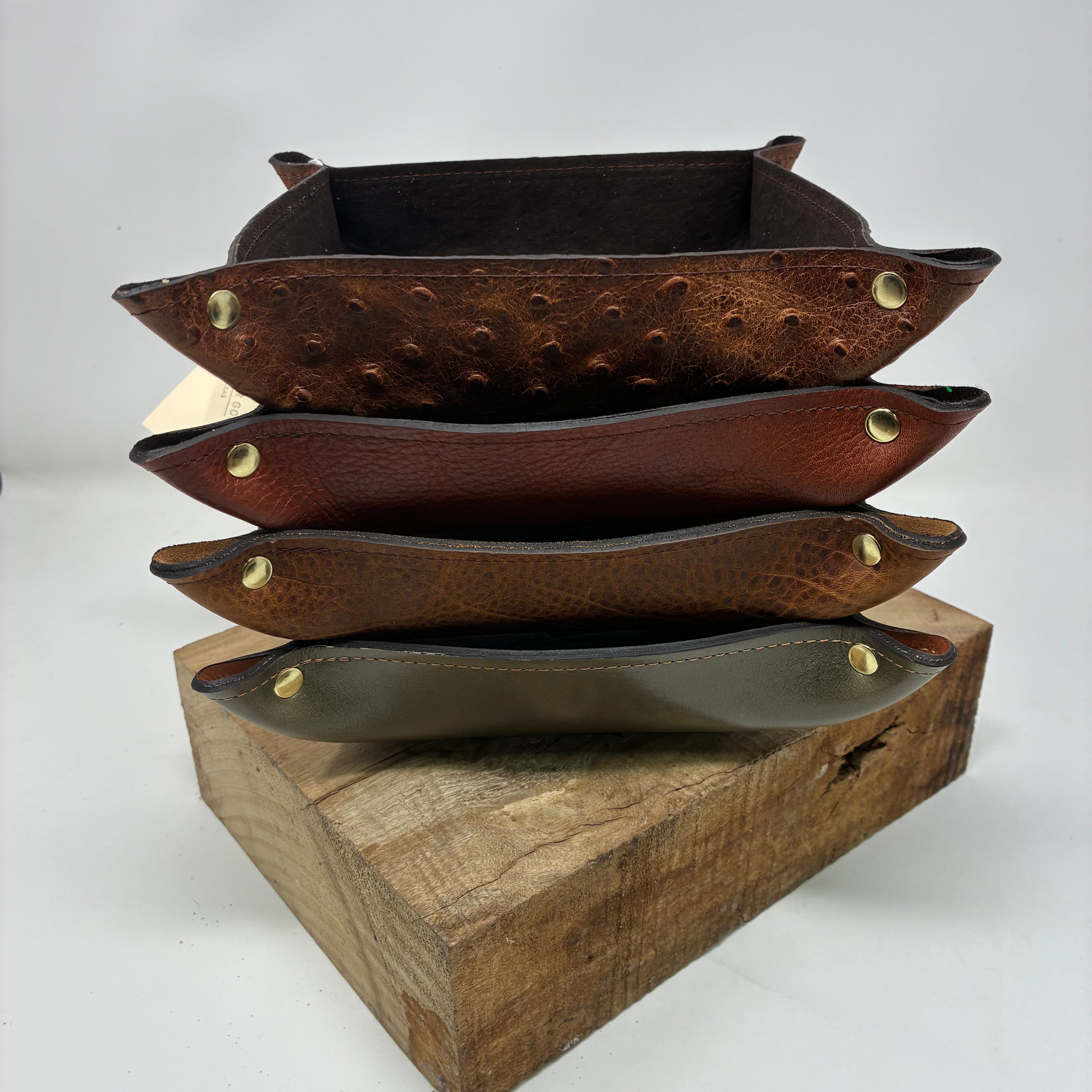 Stack of brown leather trays with gold rivets on a wooden block against a white background